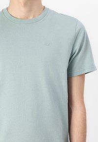 Ανοιχτό μπλε βαμβακερό T-shirt με στρογγυλή λαιμόκοψη, κοντά μανίκια και διακριτό κεντητό λογότυπο στο στήθος. Λείο ύφασμα, άνετη εφαρμογή.