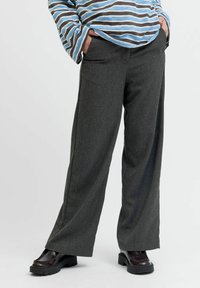 Pantalons larges gris avec une texture subtile, dotés de poches latérales et d'une silhouette droite. Associés à des chaussures noires à semelle épaisse.