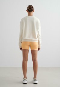 Felpa oversize crema con spalle abbassate, abbinata a pantaloni corti arancio chiaro. Design semplice, texture liscia e colori a contrasto.