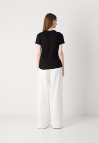 T-shirt nera a maniche corte con scollo rotondo, abbinata a pantaloni bianchi a gamba larga con tasche posteriori e una trama di tessuto liscia.