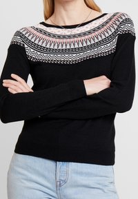 Svart tröja med ett färgglatt geometriskt mönster längs halslinningen, med långa ärmar och ribbade mudd och nederkant.