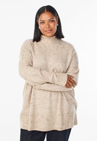 Beige, gestrickter Pullover mit hohem Kragen, gerippten Bündchen und Saum. Hat eine gesprenkelte Textur mit schwarzen Flecken. Lockerer, übergroßer Schnitt.