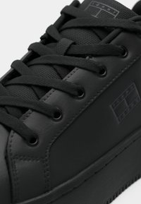 Baskets en cuir noir avec lacets noirs, languette texturée et logo discret embossé sur le côté près de la semelle.