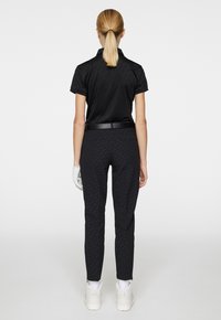 Svart pikétröja med korta ärmar och texturerad design, kombinerad med svarta smala byxor med ett subtilt mönster och vita sneakers.