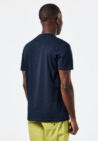 Tricou din bumbac bleumarin cu mâneci scurte, guler rotund și o textură fină, purtat cu pantaloni scurți galbeni strălucitori. Design curat, fără logo-uri vizibile.