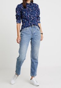Floral navy button-up shirt with long sleeves paired with light blue straight-leg jeans and white sneakers.