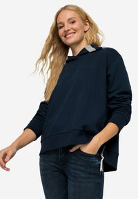 Mörkblå huvtröja med avslappnad passform, har sidodragkedjor, ribbade ärmslut och en mjuk yta. Bärs med mörka jeans.