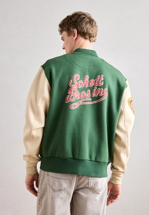 Grøn og beige varsity-jakke; har stort pink "Schott Bros inc" tekst på ryggen; blød stof, ribbede manchetter og liv.