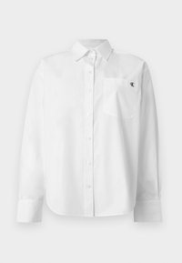 Λευκό μακρυμάνικο πουκάμισο με κουμπιά, μυτερό γιακά και μπροστινή τσέπη με μικρό μαύρο λογότυπο "CK" στο αριστερό στήθος.