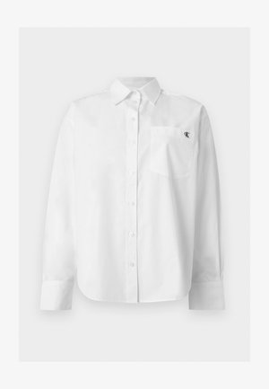 Λευκό μακρυμάνικο πουκάμισο με κουμπιά, μυτερό γιακά και μπροστινή τσέπη με μικρό μαύρο λογότυπο "CK" στο αριστερό στήθος.