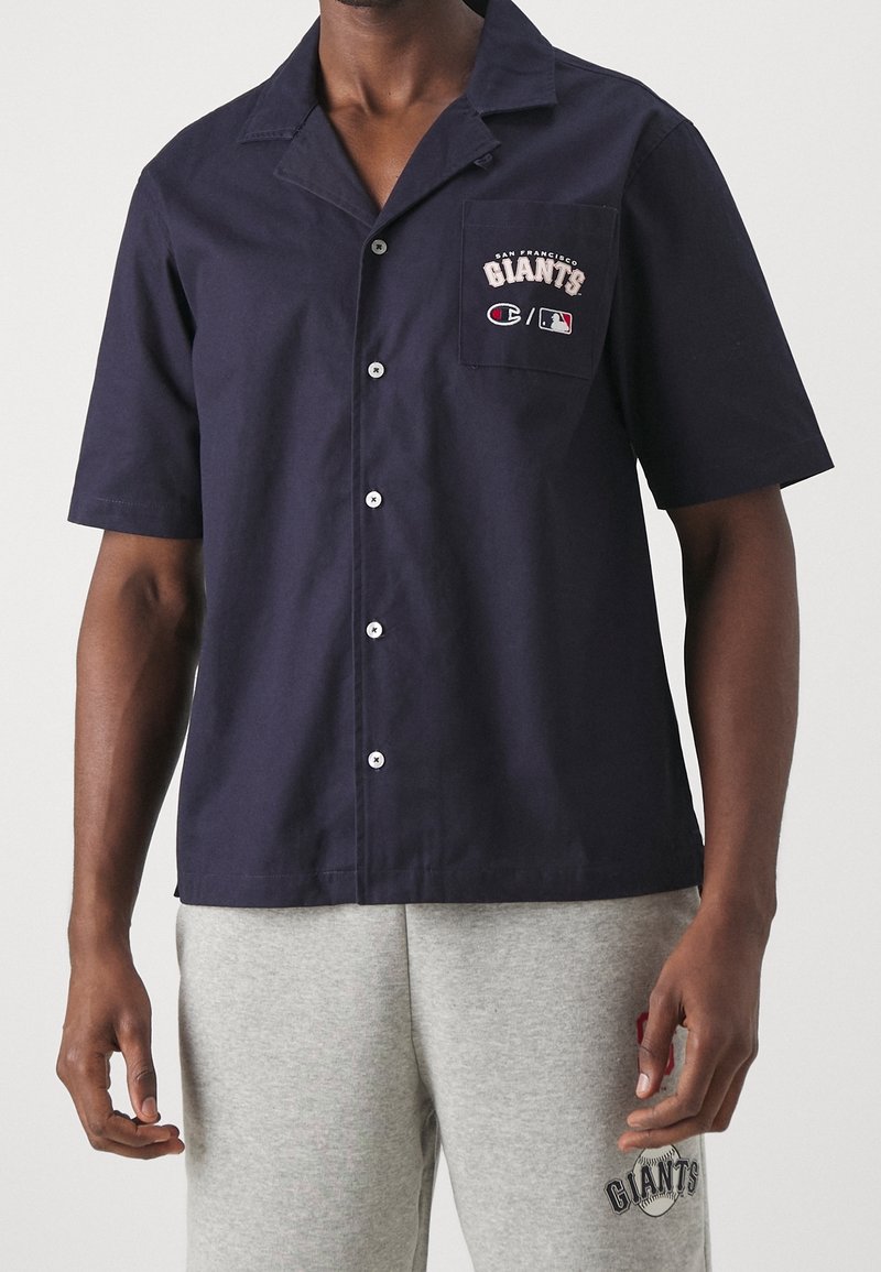 Marineblauw shirt met korte mouwen van katoen met een kraag, voorzien van een voorzak geborduurd met "San Francisco Giants" in wit en rood.