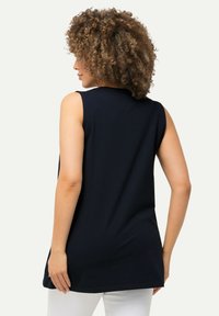 Top nero senza maniche realizzato in un tessuto morbido, con una vestibilità comoda e orlo arrotondato. La vista posteriore mostra un design semplice senza decorazioni visibili.