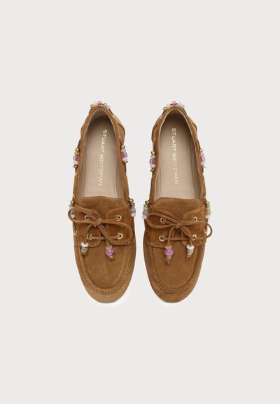 Paire de mocassins en daim marron avec nœuds en dentelle et perles décoratives roses et blanches sur les bords et les lacets, nom de la marque visible à l'intérieur.