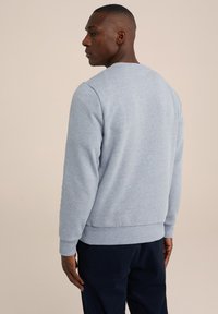 Sudadera gris claro de cuello redondo con puños y dobladillo acanalados, hecha de una tela suave. Presenta una textura lisa y un diseño minimalista.