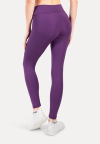 Fioletowe legginsy z wysokim stanem, wykonane z elastycznej tkaniny, dopasowany krój, gładka faktura, połączone z białymi butami sportowymi.