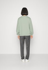 Felpa verde chiaro con polsini e orlo a coste, abbinata a pantaloni grigi su misura e sneaker bianche. Cuciture visibili e vestibilità rilassata.