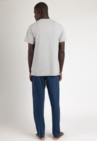Camiseta de algodón gris con mangas cortas y cuello redondo, combinada con pantalones ligeros azul marino. Diseño simple, sin patrones notables.