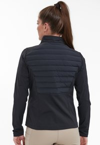 Giacca nera con un design aderente, caratterizzata da un pannello posteriore trapuntato. Il tessuto appare liscio con maniche lunghe. Solo vista posteriore.