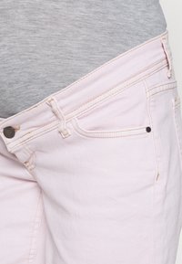Jeans de ganga cor-de-rosa claro com cintura alta, apresentando fecho de botão, passantes para cinto e bolsos frontais. A textura é suave com um ligeiro brilho.
