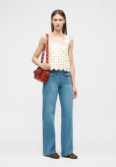 Femme portant un haut en crochet blanc, un jean taille haute bleu, des ballerines à imprimé léopard et un sac à bandoulière en cuir rouge.