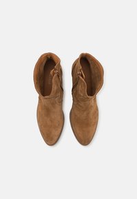 Botas de ante marrón hasta el tobillo con punta afilada y cremalleras laterales. Textura suave con un tacón bajo y líneas limpias, que muestran un diseño minimalista.