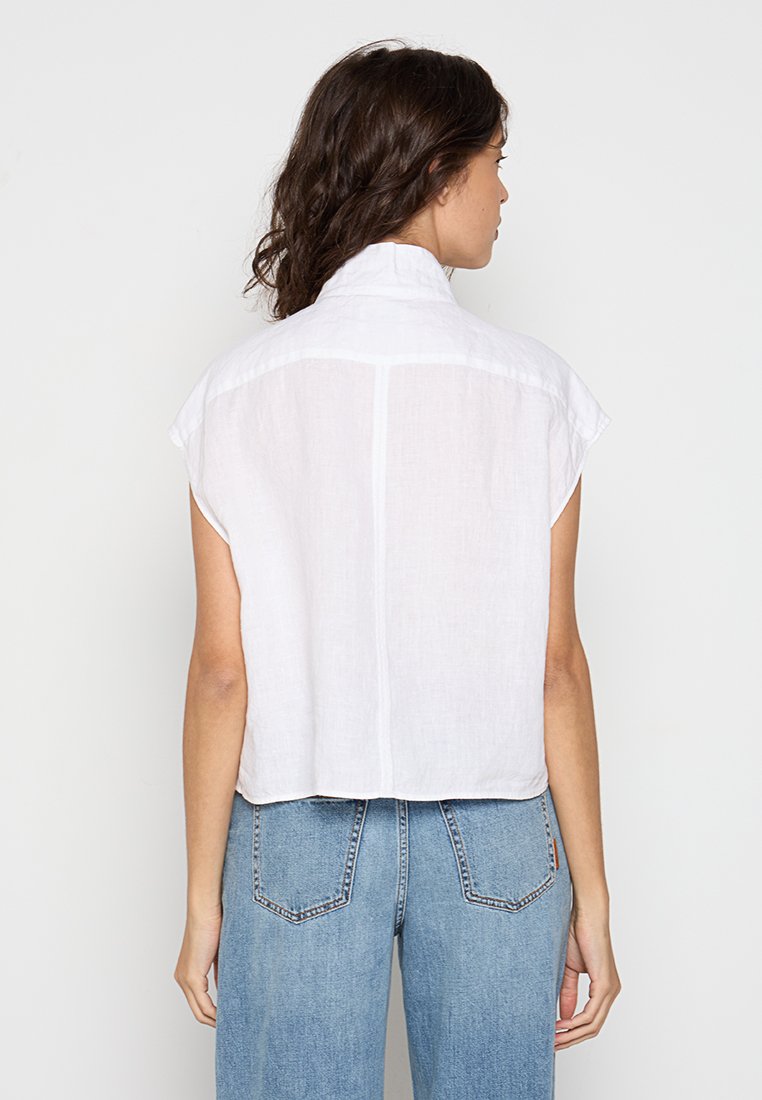 Weißes Leinenhemd mit kurzen Ärmeln, Rückenpasse, cropped Design und subtiler Struktur. Kombination mit hoch-taillierten blauen Denim-Jeans.