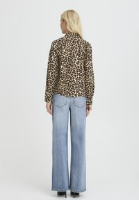 Bluză cu imprimeu leopar, cu guler, mâneci lungi și croială lejeră, purtată împreună cu blugi de culoare albastru deschis, cu croială largă, și pantofi cu toc negri.