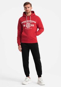 Röd hoodie med vit grafisk text, dragsko i huvan och framfickan. Matchas med svarta joggers och vita sneakers.