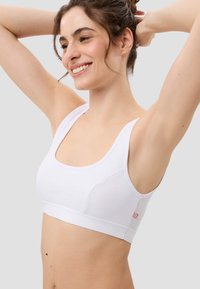 Weißer Sport-BH mit breiten Trägern, quadratischem Ausschnitt und strukturierten Seitenpaneelen. Besitzt ein dezentes Markenlogo in Pink am Bund.