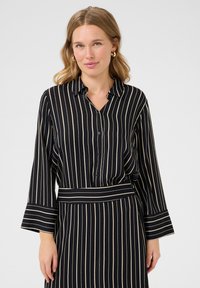 Abito camicia con bottoni, strisce verticali bianche e nere, maniche lunghe e vita regolabile con cintura. Tessuto morbido con una trama liscia.