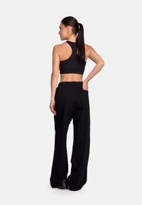 Top sportiv negru, scurt, cu spate tip racer, combinat cu pantaloni negri, largi, care au un buzunar lateral, pe un fundal neutru.