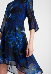 Kurzes Kleid aus durchsichtiger Stoff, mit einem blauen und grünen Blumenmuster, einem fließenden Saum und einer lockeren Passform.