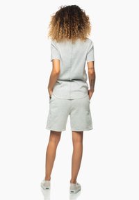 Světle šedý krátký overal s volným střihem, vybavený neviditelným zipem a bočními kapsami, doplněný neutrálními teniskami.