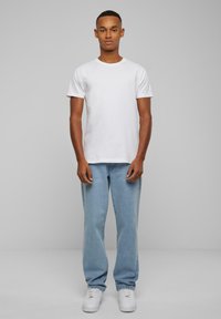 Hvit bomull T-skjorte med korte ermer, kombinert med lyseblå denimjeanser og hvite joggesko, stående mot en grå bakgrunn.