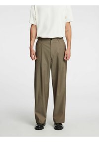 Brūnas kroku bikses ar piegriezumu, ar vienu pogu aizdari, kabatām un gludu tekstūru. Valkātas kopā ar baltu kreklu.