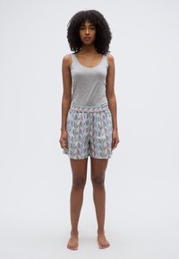 Γκρι αμάνικη φανέλα και πολύχρωμα σορτς με χαλαρή εφαρμογή· τα σορτς διαθέτουν ελαστική ζώνη μέσης και διαφορετικά σχέδια ζιγκ-ζαγκ.