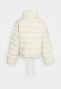 Avkortad puffjacka i krämfärg, med hög krage, boxig form, quiltad textur och justerbara snören längst ner för passform.