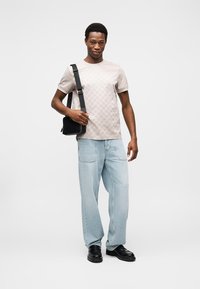 Μπεζ t-shirt με διακριτό σχέδιο και κοντά μανίκια, ανοιχτό μπλε χαλαρά τζιν και μαύρα παπούτσια. Μικρή μαύρη τσάντα ταχυδρόμου φορεμένη διαγώνια στον ώμο.