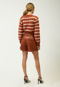 Gestreifter Pullover in Rosttönen aus flauschigem Material, kombiniert mit hochgelegten braunen Leder-Shorts mit umgeschlagenen Säumen und Gesäßtaschen. Absatzsandalen.