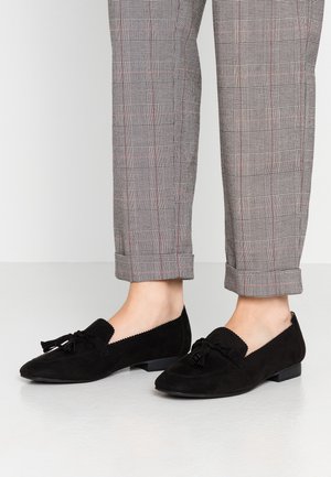 Sorte loafers i ruskind med flad hæl, prydet med en sløjfe, bølgede kanter og en mandelformet tå, kombineret med ternede bukser.