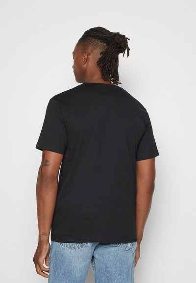 Svart bomulls T-skjorte med korte ermer, rund hals og avslappet passform. Baksiden har ingen distinkte mønstre eller detaljer. Båret med lyseblå jeans.