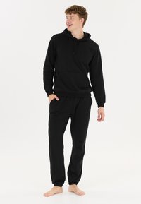Schwarzer Baumwoll-Hoodie und passende Jogginghose. Der Hoodie hat eine Vordertasche und einen Kordelzug, während die Jogginghose einen elastischen Taillenbund hat.