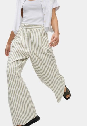 Pantalons larges rayés en beige clair et blanc cassé, avec une taille haute, des plis et une coupe décontractée, associés à un débardeur blanc.