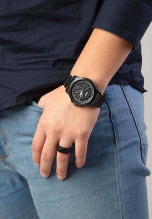 Analog wristwatch with a black round case, black metal band, and textured black face featuring white hour markers and subdials. Black ring on hand.