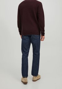 Pull à manches longues couleur marron avec un col rond, associé à un jean en denim bleu. Le pull présente un tissu texturé et des poignets côtelés, vue de dos.