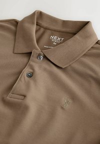 Polo marron slim fit avec col rabattable, deux boutons, et un petit logo brodé de cerf sur la poitrine.