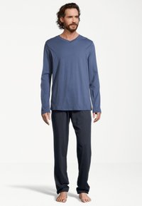 Blå langærmet V-hals skjorte parret med mørke bukser. Stoffet ser blødt og let ud, hvilket giver en behagelig pasform.