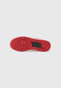 Piros gumiból készült Nike sneaker talp, körkörös és lineáris futófelületi mintákkal. Fekete logómatrica található a saroknál.