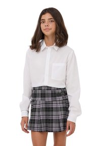 Camicia bianca a maniche lunghe con bottoni, dotata di una singola tasca sul petto, abbinata a una gonna a quadretti nera e viola con design a pieghe.