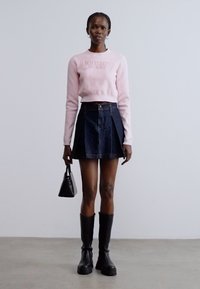 Maglione rosa lavorato a maglia con scritta "Tommy Jeans", abbinato a una gonna di jeans scura. Stivali neri al ginocchio e una piccola borsa nera completano il look.